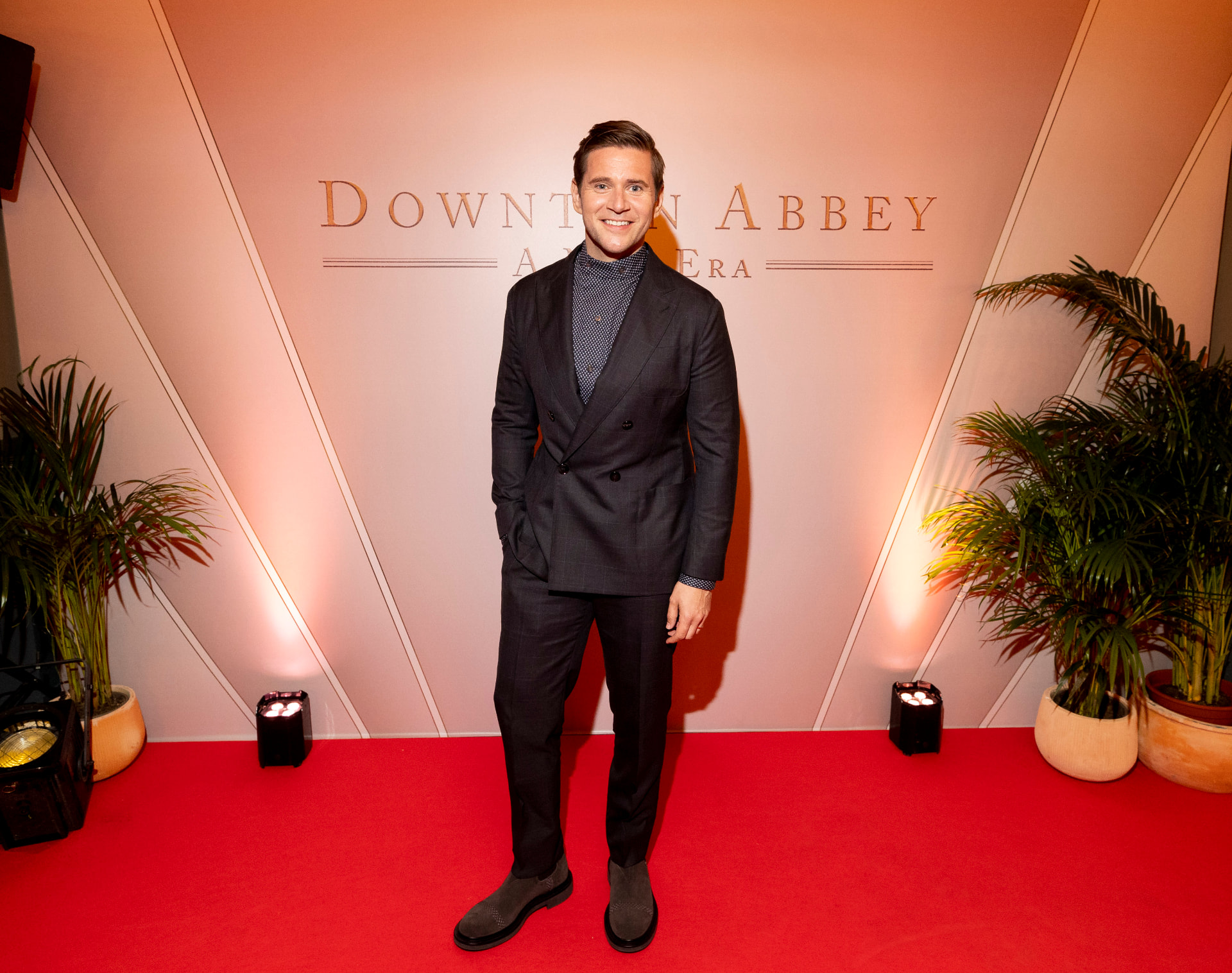 Guest in a dark double-breasted suit posing on the red carpet at Downton Abbey: A New Era